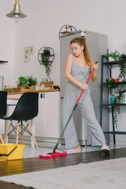 Close-up of people cleaning wooden floor with broom and dustpan indoors.
